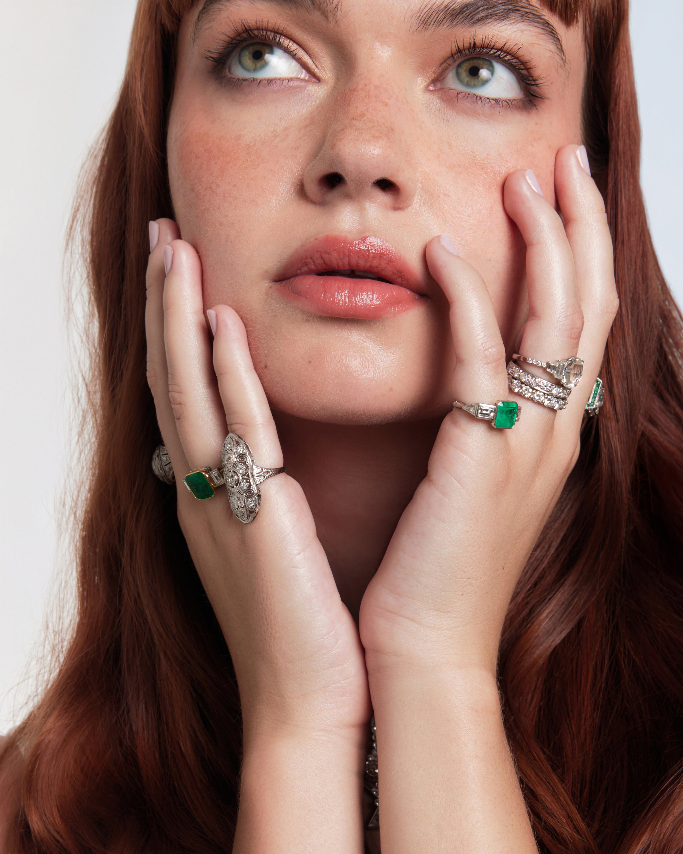 Woman wearing multiple rings with green gemstones on a plain background