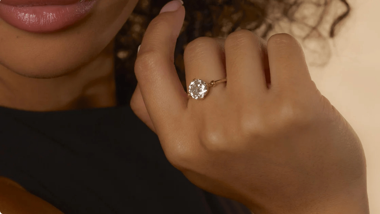 A close-up of a woman gently touching her face, showcasing a Victorian-era Old European cut diamond engagement ring set in 18k yellow gold.